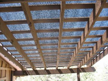 Black knit shade fabric attached to the top of a wood pergola patio trellis with plastic locking clips