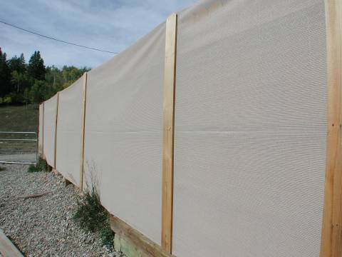 Knit shade fabric in 6 foot width attached to the 'ugly side' of a cedar wood slat fence in yard for windbreak