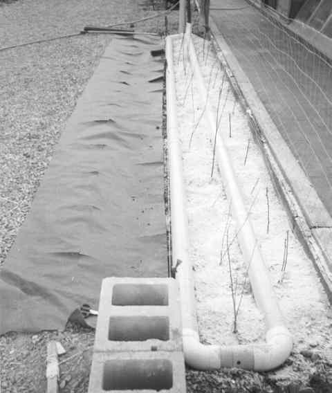 Perforated pipe installed underneath woven geotextile fabric for an outdoor greywater or roof-runoff planterbed