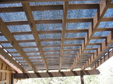 90% black knit shade fabric attached to the top of a wood pergola patio trellis with plastic locking clips