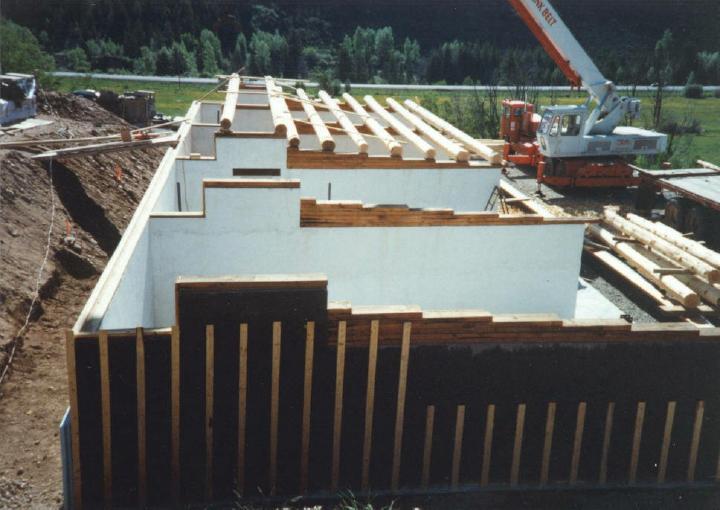 Round log purlins going in over the top of interior HTM walls with stepped timbers to set roof slope