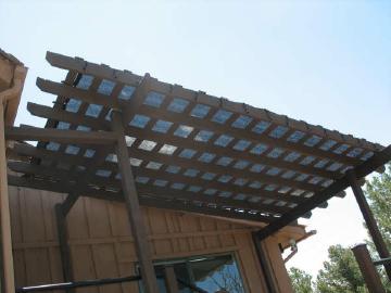 Black knit shade fabric attached to the top of a wood pergola patio trellis with plastic locking clips